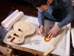 mid adult man at work as craftsman in italian workshop with guitars and blueprints, drawing sketches. high angle view