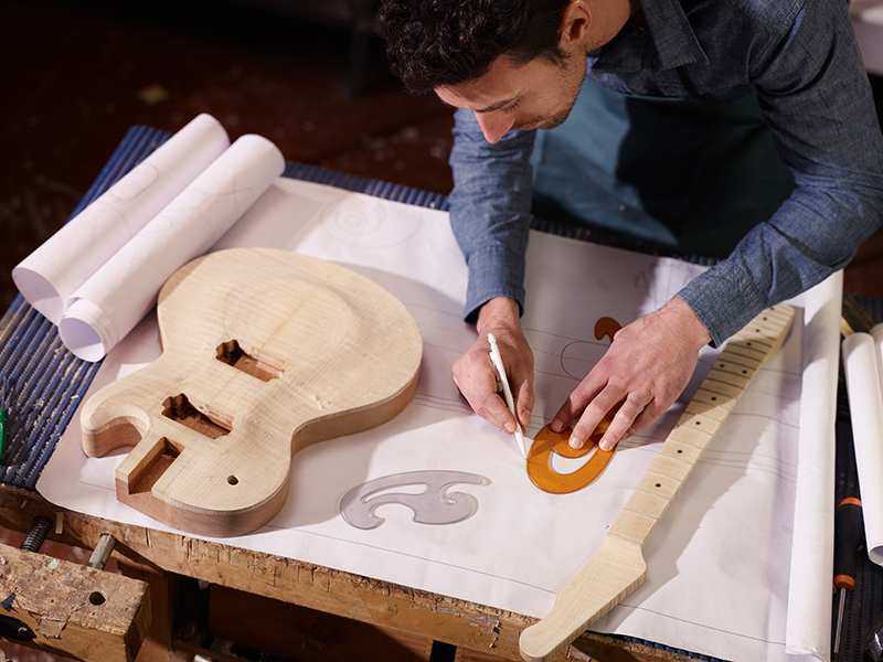 mid adult man at work as craftsman in italian workshop with guitars and blueprints, drawing sketches. high angle view