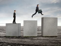 Businessmen on stone cubes jumping towards higher ones