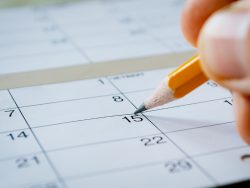 Person marking the date of the 15th with a pencil on a blank calendar with date squares as a reminder of an important day or to schedule a meeting or event
