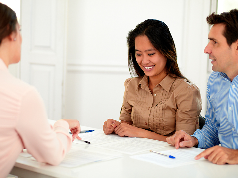 Portrait of young couple working with financial advisor while smiling and sitting on assistance workplace