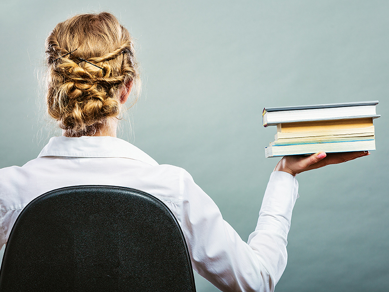 Education school or business concept. Woman female student sitting on chair holding stack books. Back view grunge background