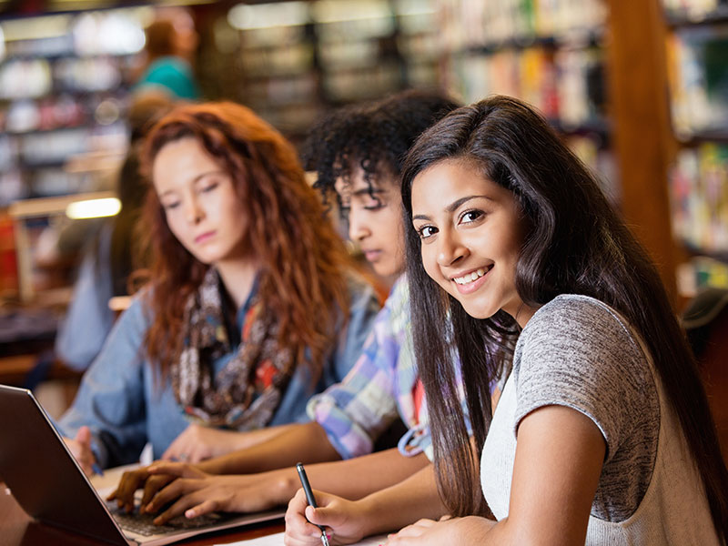 Indian teen studying in library with college age friends