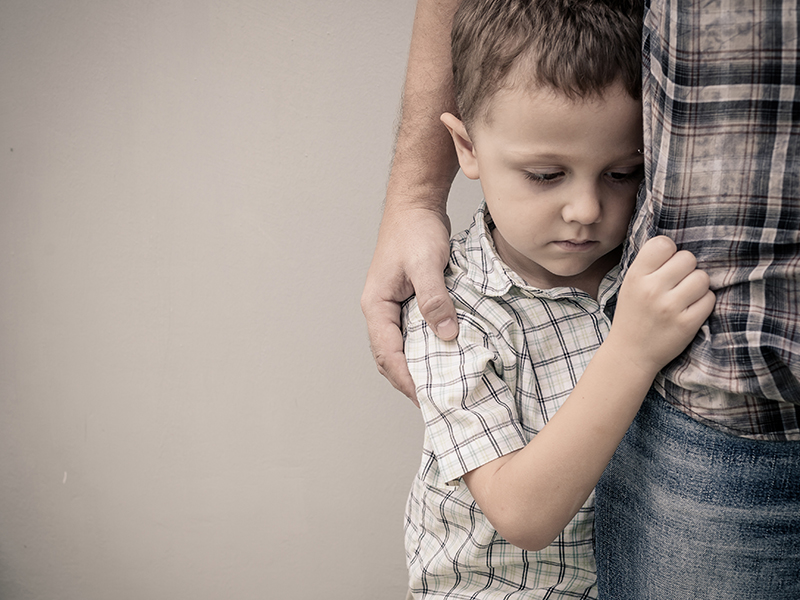 sad son hugging his dad near wall at the day time