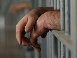 mans hands behind bars in jail or prison