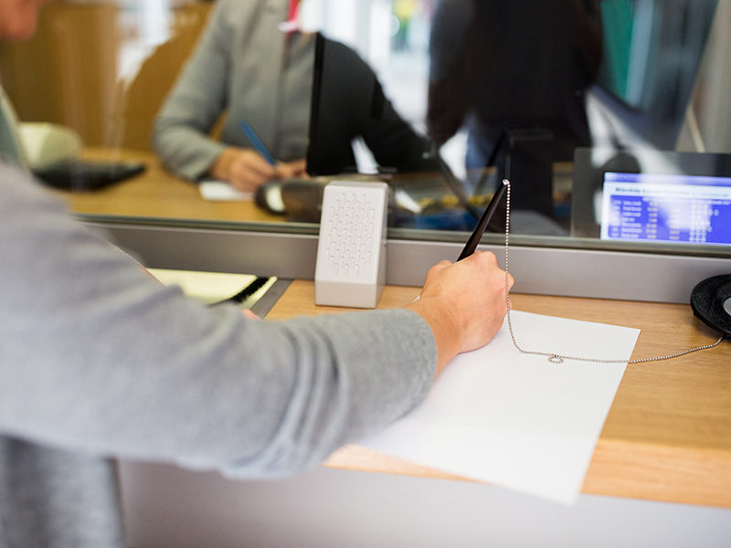 people and finance concept - customer with pen and paper writing application at bank office