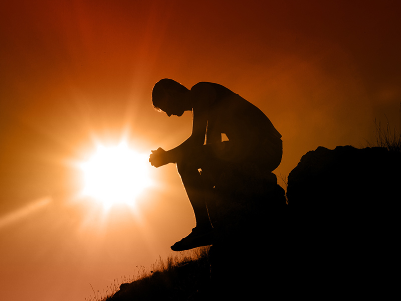 Man sitting on hill sunset in background