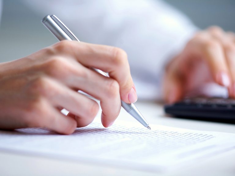 photo of hands holding pen under document and pressing calculator buttons