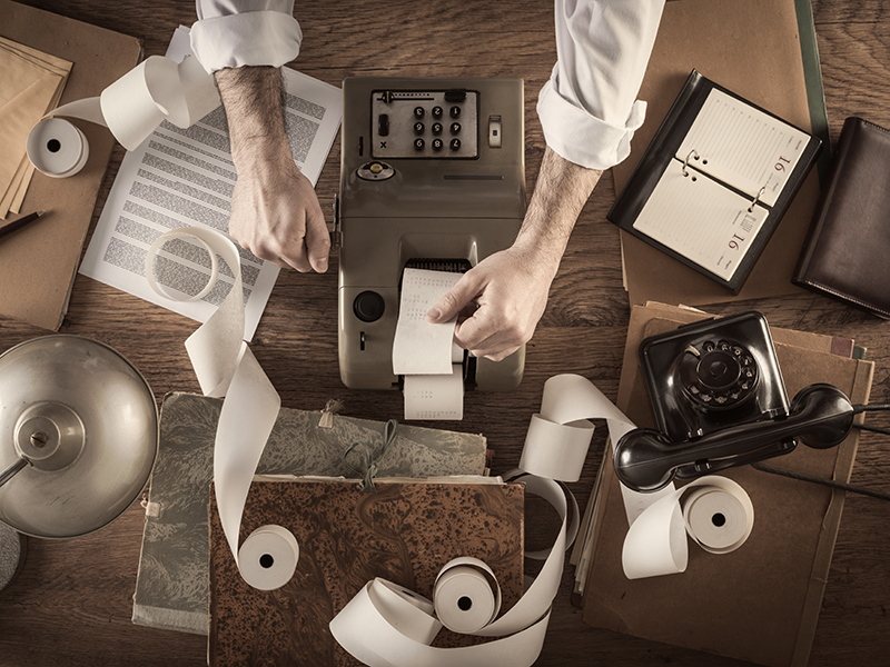 Messy vintage accountant's desktop with adding machine and paper rolls, he is working with the calculator