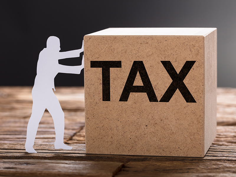 Closeup of paper man pushing tax wooden block on table against gray background