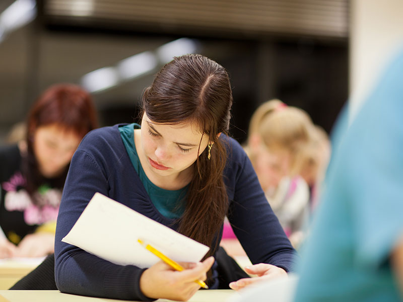 Pretty female college student sitting in a classroom full of students during class