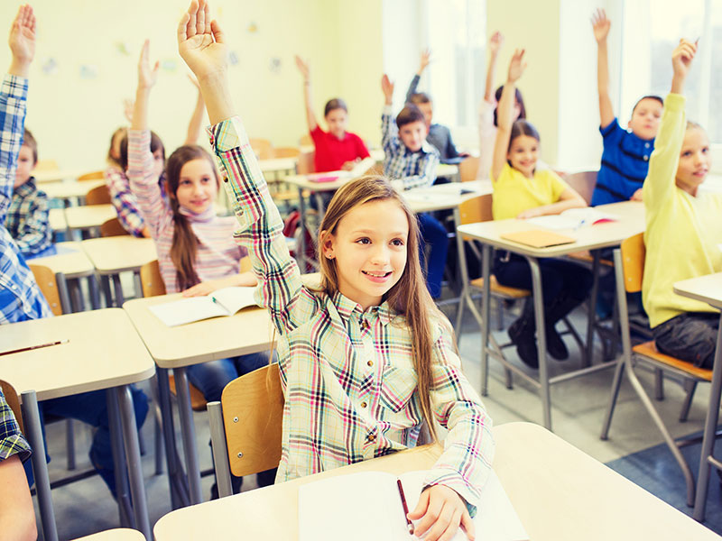 education, elementary school, learning and people concept - group of school kids with notebooks sitting in classroom and raising hands