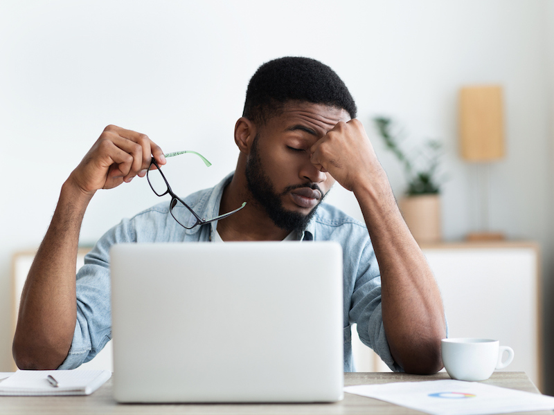 Tired african american employee having headache after working on laptop in office, copy space