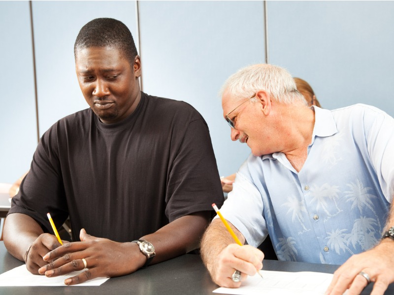 Older college student trying to copy off a younger student's test paper