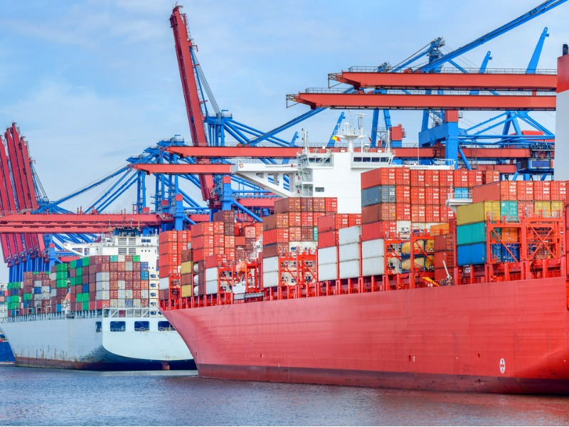 Three cargo ships with shipping containers docked at the container terminal in the port of Hamburg.