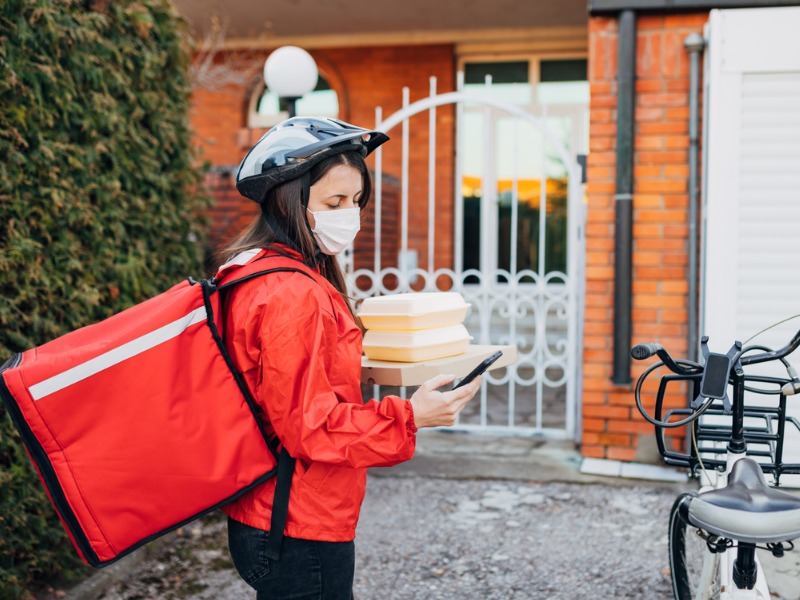 Female bike delivery person, checking the address on the mobile phone, on the delivery app,